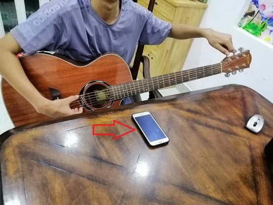 Cần đặt điện thoại ở vị trí gần lỗ thoát âm của đàn guitar để dễ dàng cho quá trình lên dây đàn guitar.